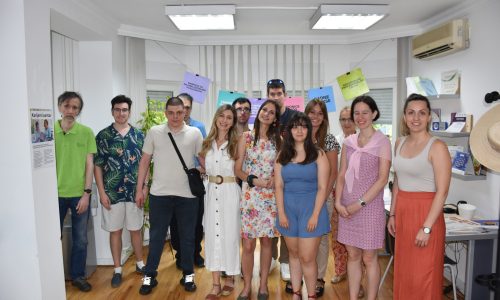 Grupna fotografija učesnika i učesnica FMI razgovora na temu data analize u bankarstvu, snimljena u prostoru Karijernog centra. Ljudi stoje nasmejani ispred postera sa natpisima koji promovišu aktivnosti centra, kao što su treninzi, radionice i podrška u zapošljavanju.